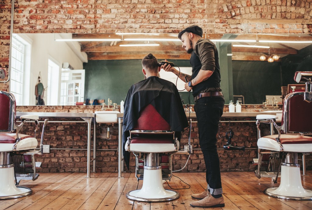 Rear view of a male hairdresser cutting a client's hair in a barber shop