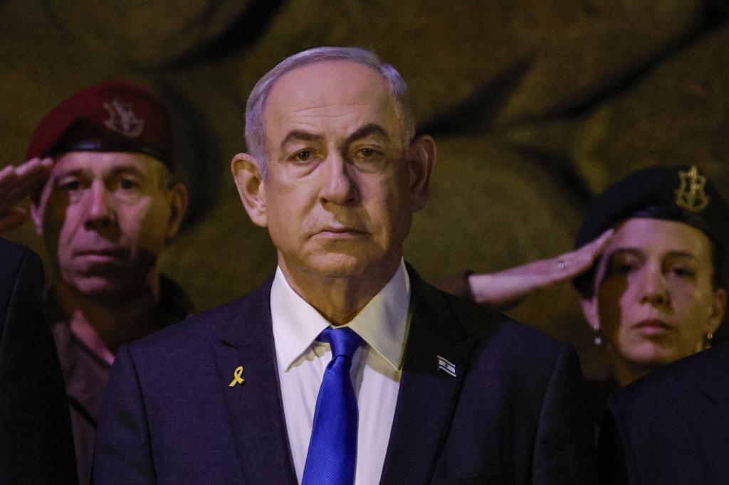 Israel Prime Minister Benjamin Netanyahu stands with a grim face while two Israeli soldiers behind him salute.