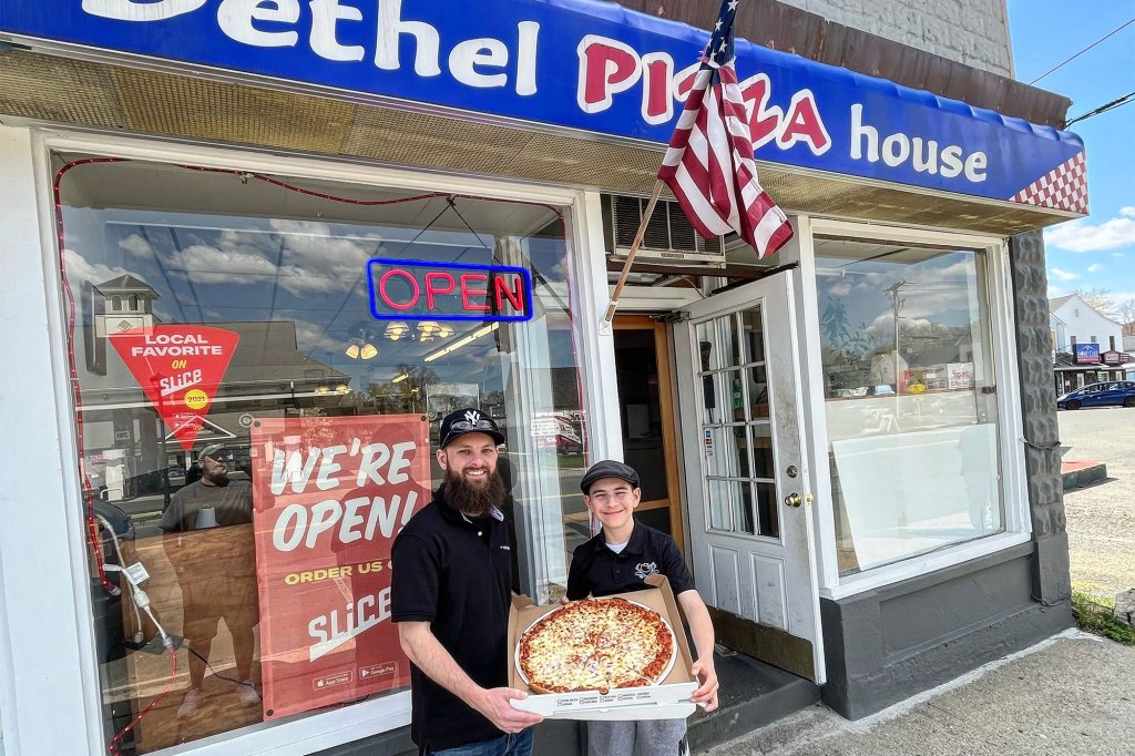 A man and boy holding a pizza box in front of a pizza shop