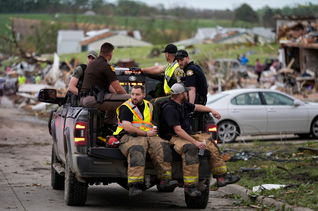 Law enforcement officers and firefighters ride in a truck past homes in Greenfield, Iowa.