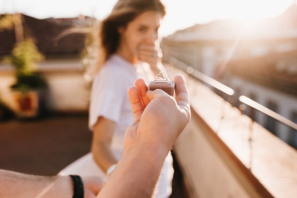 Man proposing to astonished woman on rooftop during evening