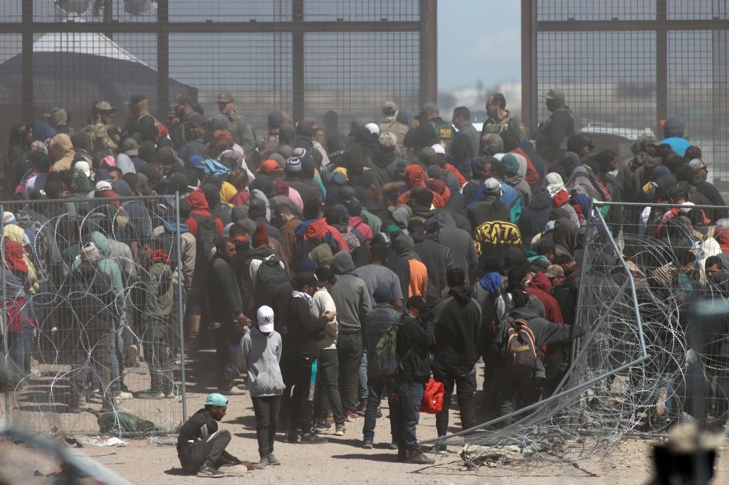 Hundreds of migrants break through a wire fence and approach the border wall