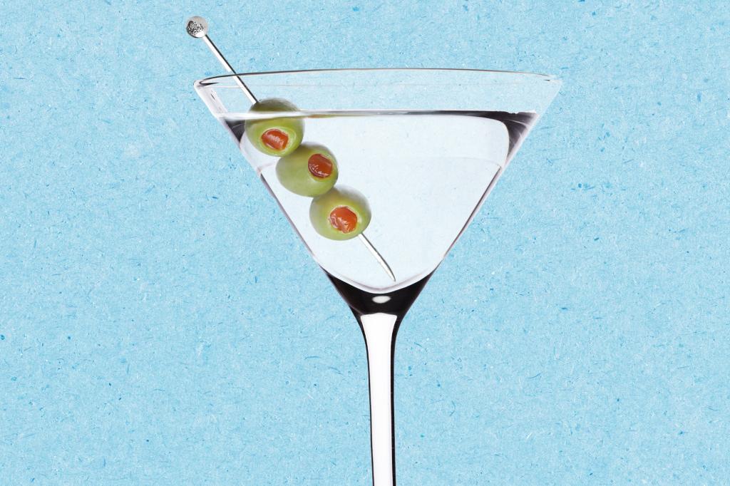 A martini glass with olives on a stick against a blue paper texture background