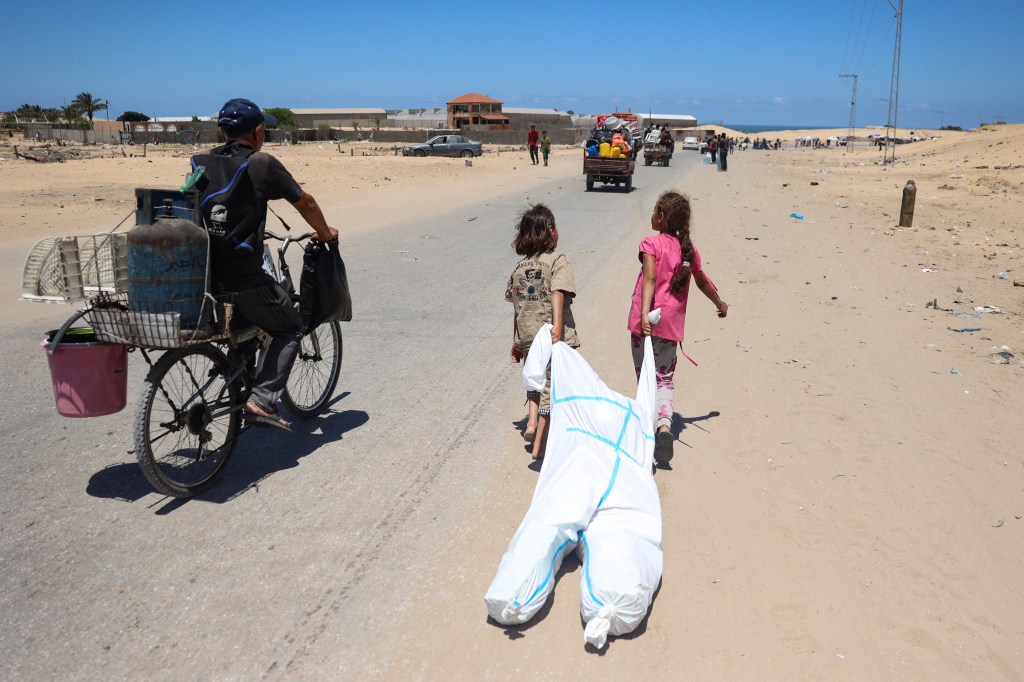 Children use a hazmat suit to carry their belongings as they flee the flighting in Rafah.