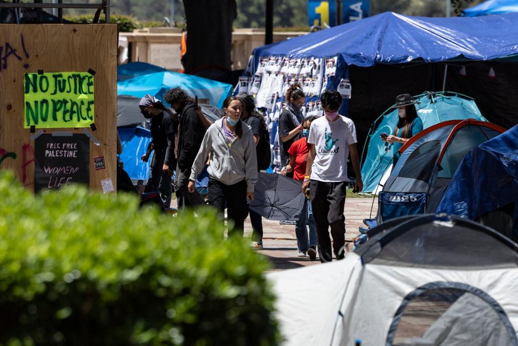 People walking through a pro-Palestinian protest encampment at UCLA campus with police cars in the background