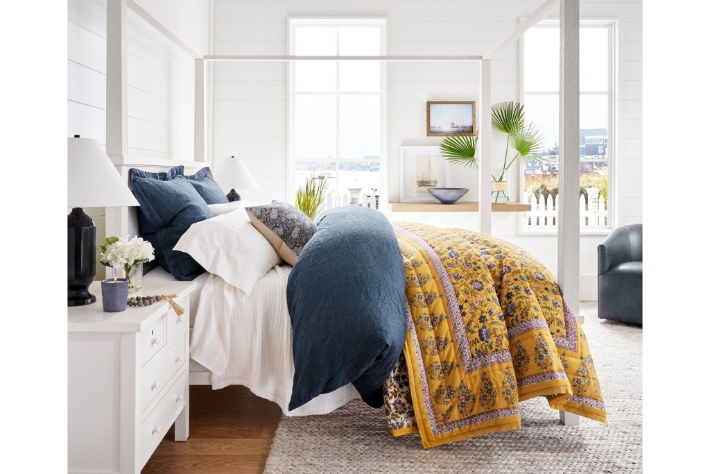 A bed with a yellow blanket and pillows in a Pottery Barn style setting