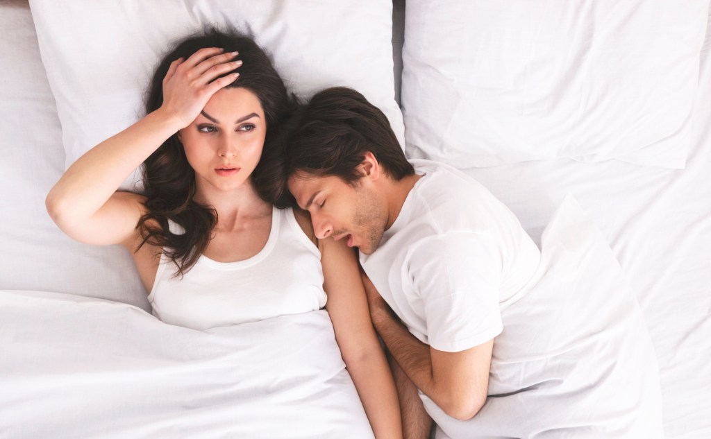 Woman in bed awake with man sleeping next to her