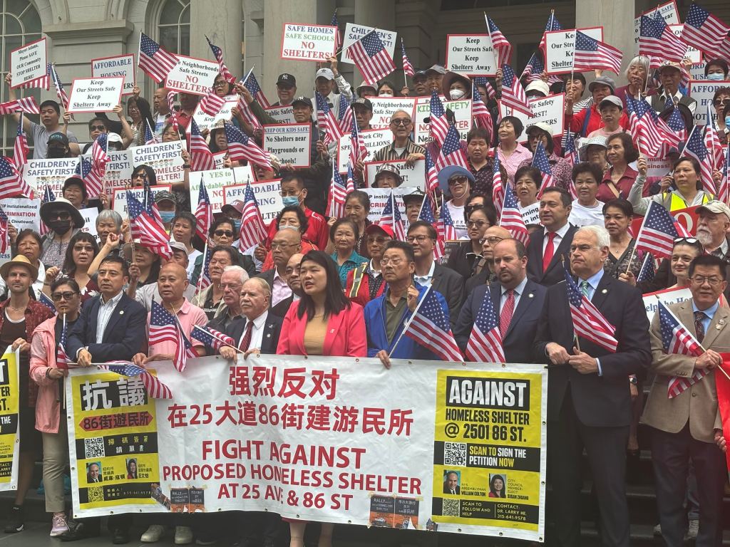 A large crowd of demonstrators lining the steps of City Hall in Manhattan, many holding signs and American flags.