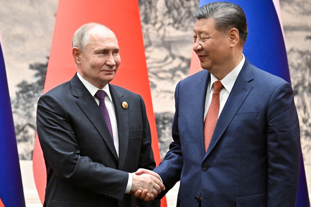 Russian President Vladimir Putin shaking hands with Chinese President Xi Jinping in Beijing, in front of a red and blue flag