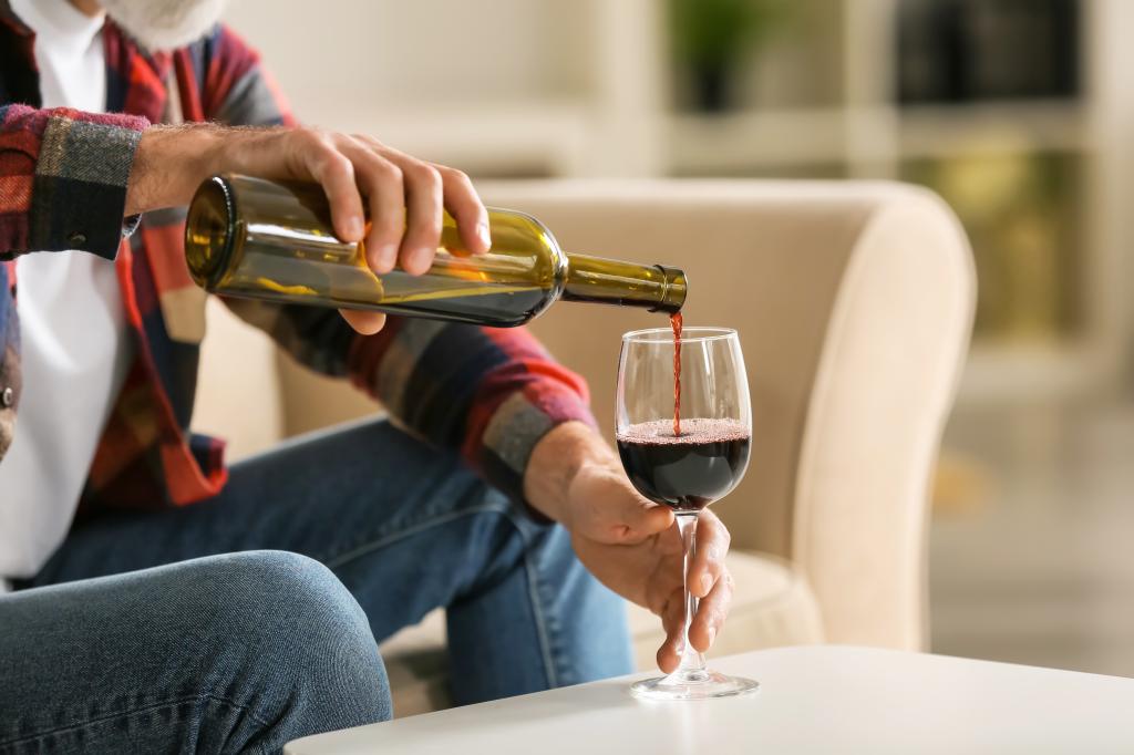 Senior man at home pouring red wine into a glass