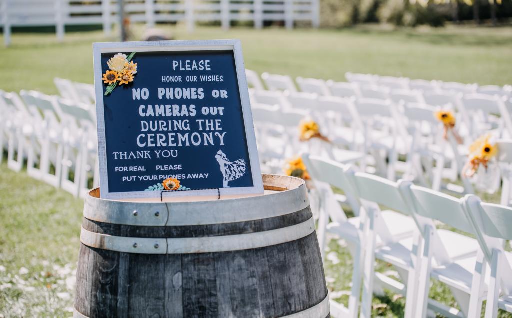 A wedding sign on a barrel requesting no cell phones, with chairs in the background