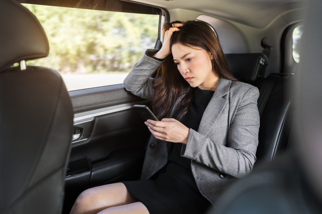 stressed young business woman using a smartphone while sitting in the back seat of car