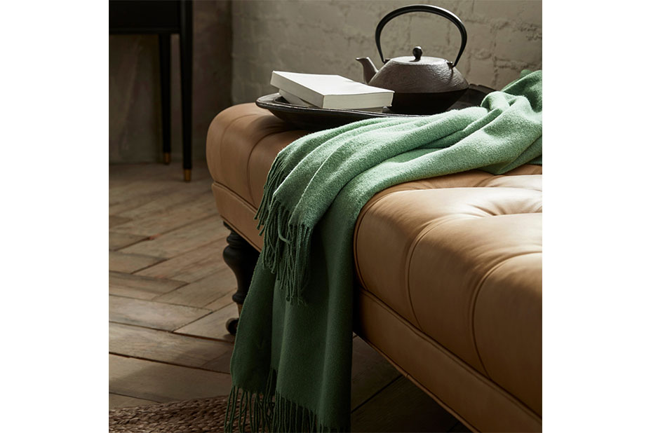 A green blanket and a tray of tea on a brown leather bench