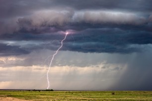 Lightning bolt striking a field during a thunderstorm with dark storm clouds
