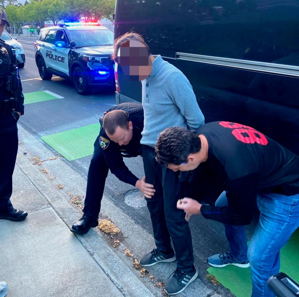 Lee is arrested by authorities who pat him down in a gutter between a sidewalk and a road in San Francisco. He is handcuffed and his face is pixilated in the police-provided picture.