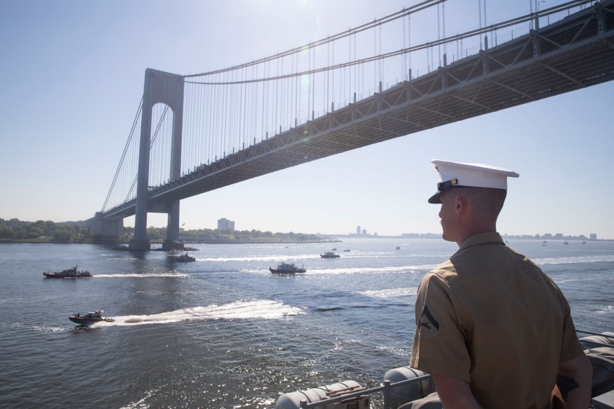 A U.S. Marines assigned to the amphibious assault ship USS Bataan (LHD 5) mans the rails as the ship passes under the Verrazzano-Narrows Bridge.