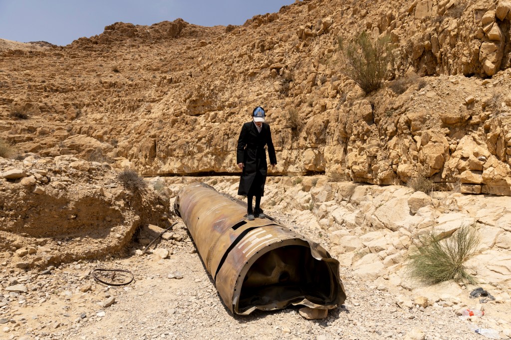 An Ultra-Orthodox Jewish boy stands on a missile debris