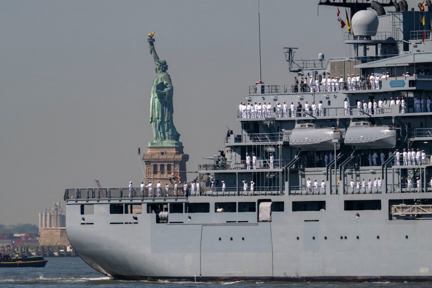 U.S. Sailors and Marines stand on the deck of the USS Bataan as it passes the Statue of Liberty.