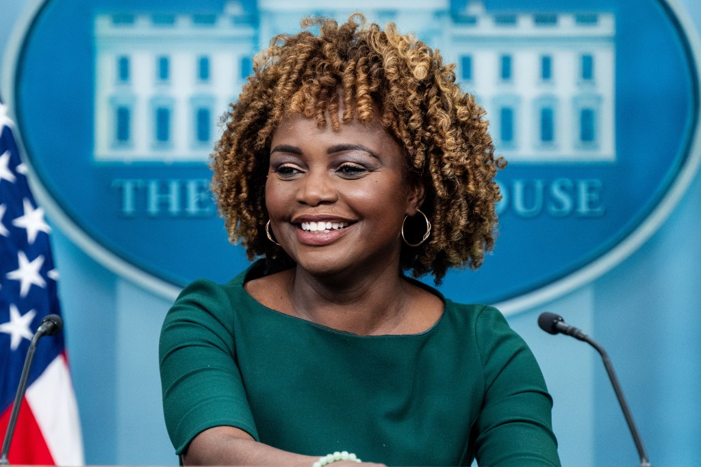 White House Press Secretary Karine Jean-Pierre speaking at a press briefing in the White House Press Briefing Room in Washington, DC, smiling at the camera