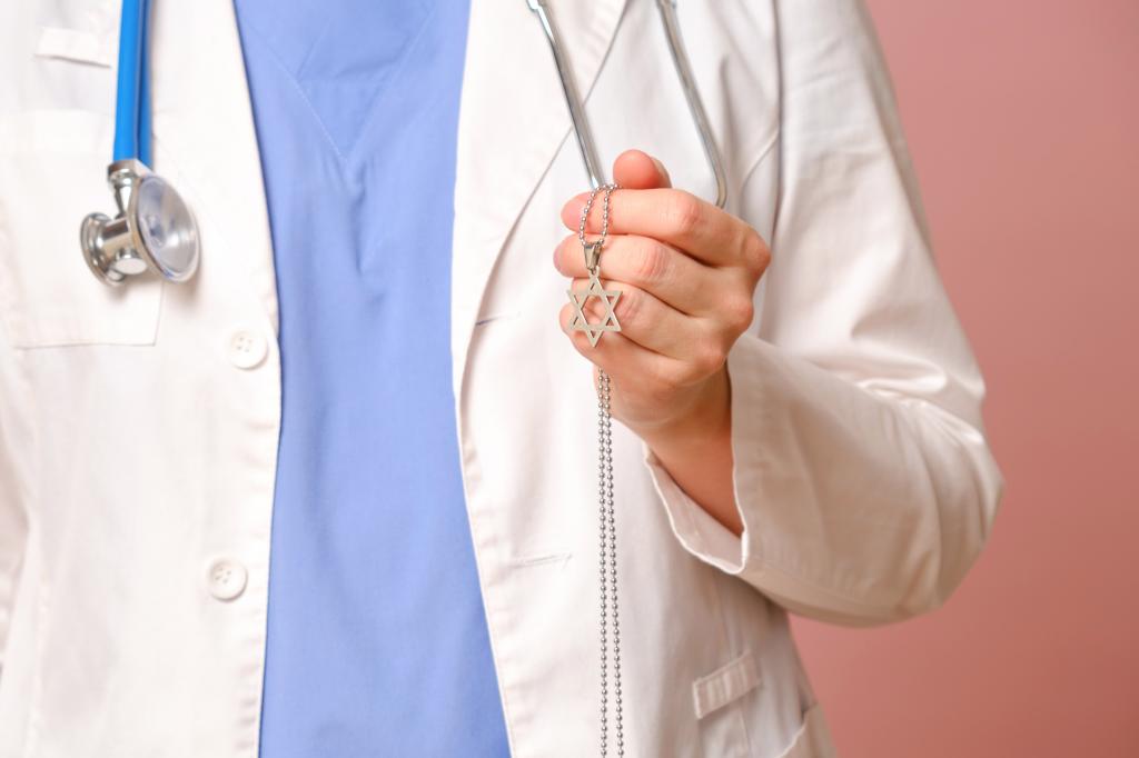 Woman doctor in white coat holding a Jewish religious symbol, posed against a pink studio background