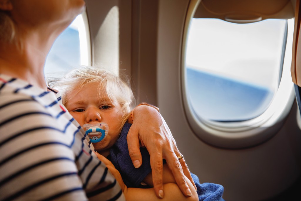 Woman holding her crying toddler child by the airplane window during travel