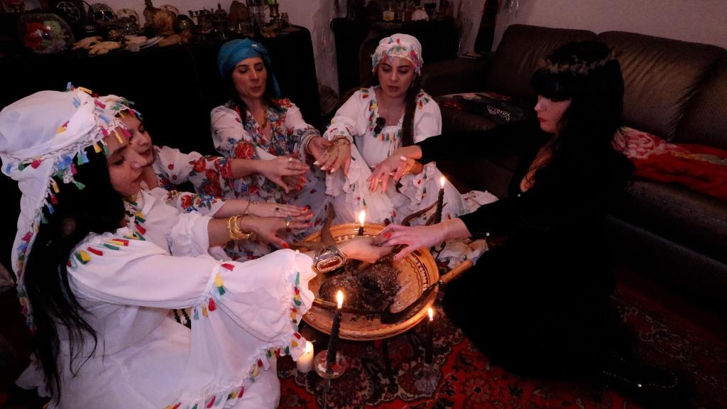 Brocarde and a group of witches in white dresses conducting a ritual around a table with candles in Romania