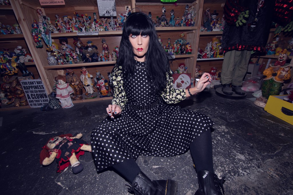 Woman named Brocarde sitting on the floor at The Clown Motel in Nevada, in front of a shelf full of dolls