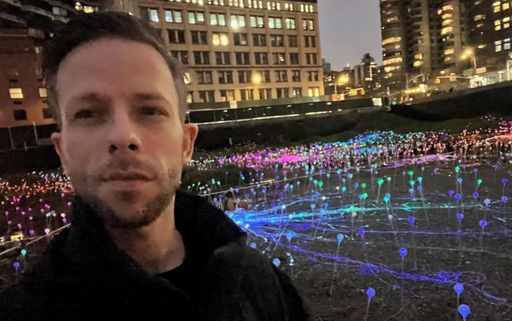 A selfie of a man in front of Field of Light's illuminated flowers. 