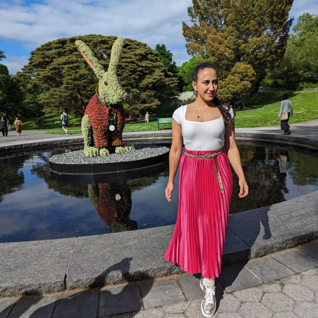 A woman dressed in a bright pink skirt poses in front of a large rabbit topiary at "Wonderland: Curious Nature" at the New York Botanical Garden.