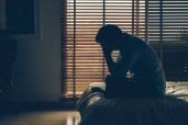 Man sitting head in hands on the bed in the dark bedroom with low light environment, dramatic concept, vintage tone color