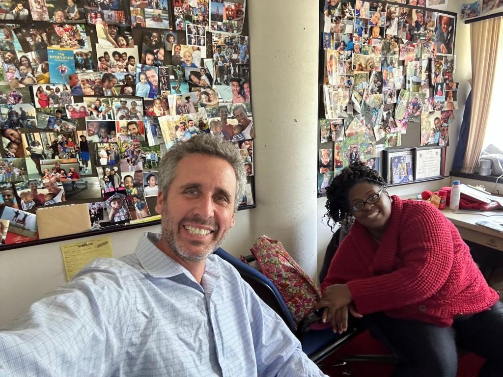 Ari Nagel and one of his baby mamas pose in front of a wall of photos he keeps of his children in his office at Kingsborough Community College