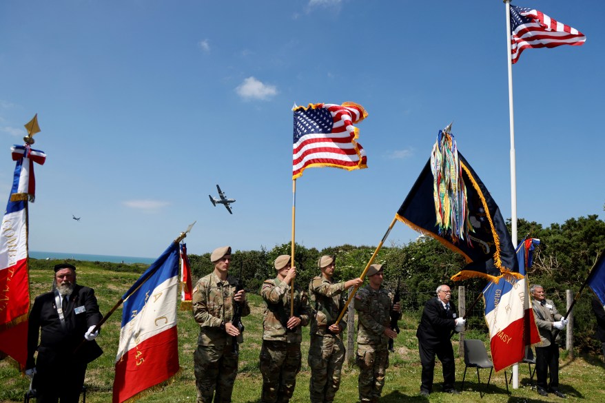 Lockheed C-130 Hercules aircraft overfly French veterans and US military soldiers as they raise flags during a ceremony on "Pointe du Hoc" clifftop in Cricqueville-en-Bessin, northwestern France, on June 5, 2024.