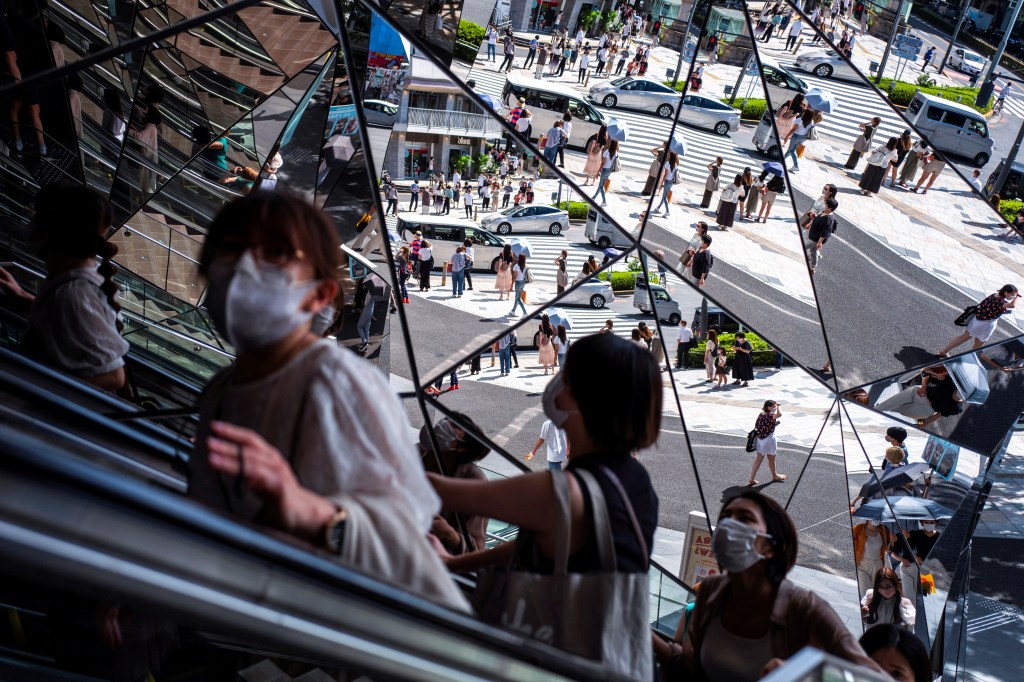 People wearing protective masks reflected in a mirror at a Tokyo shopping mall during COVID-19 outbreak