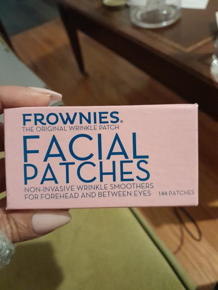 A hand holding a box of Frownies face patches for wrinkles.