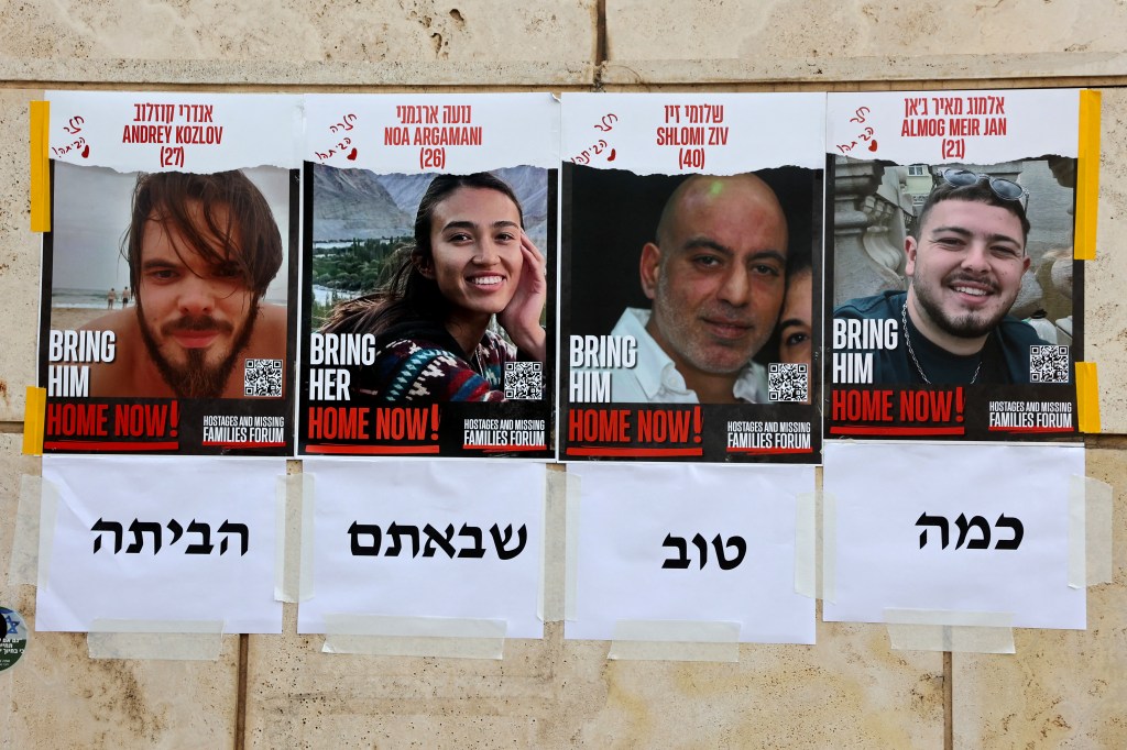 Posters on a wall in Tel Aviv, reading 'Home Now', displaying the faces of four rescued Israeli hostages: Andrey Kozlov, Noa Argamani, Shlomi Ziv, and Almog Meir Jan, taken in 2024 amid Israel-Palestinian conflict