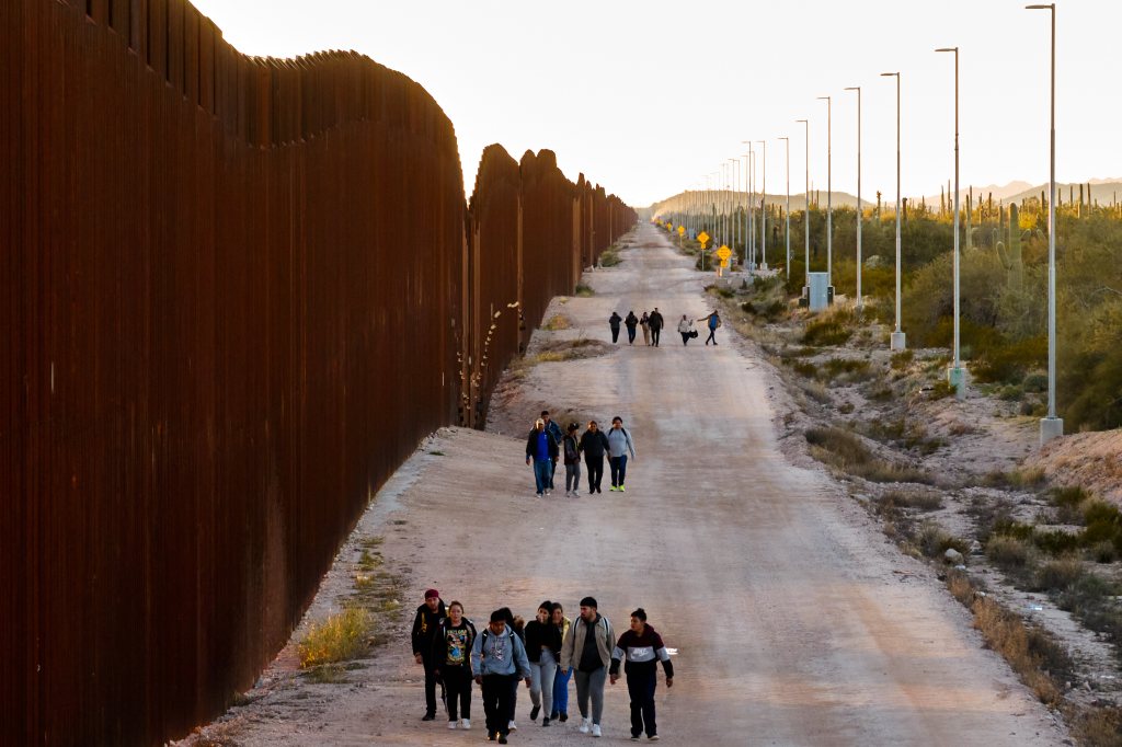 Migrants walk in small groups along the border wall to turn themselves in to Border Patrol agents in Lukeville, Arizona.