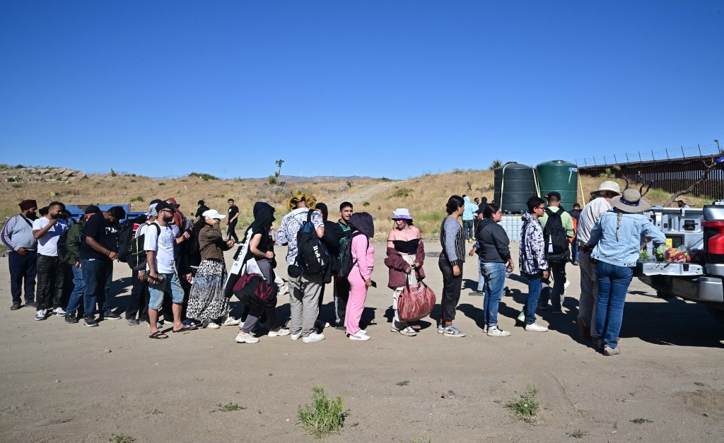 Migrants from various countries standing in line for fruit and water in Jacumba Hot Springs, California after walking from Mexico under intense heat