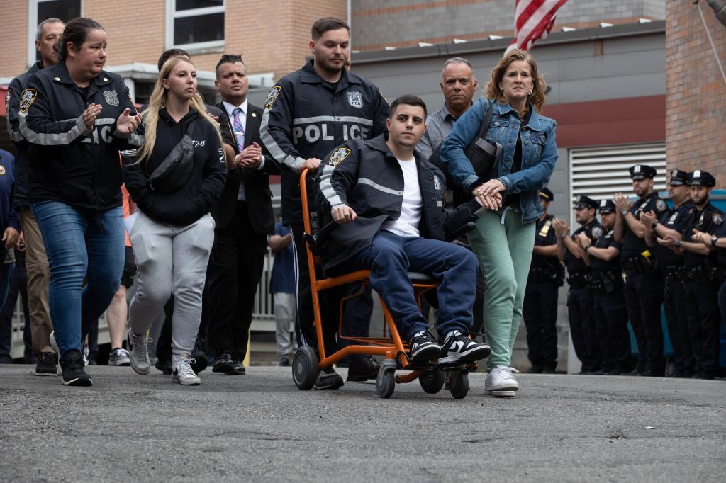 NYPD officers applaud as Officer Richard Yarusso pushes his partner Officer Christopher Abreu in a wheelchair after the pair were shot Monday.