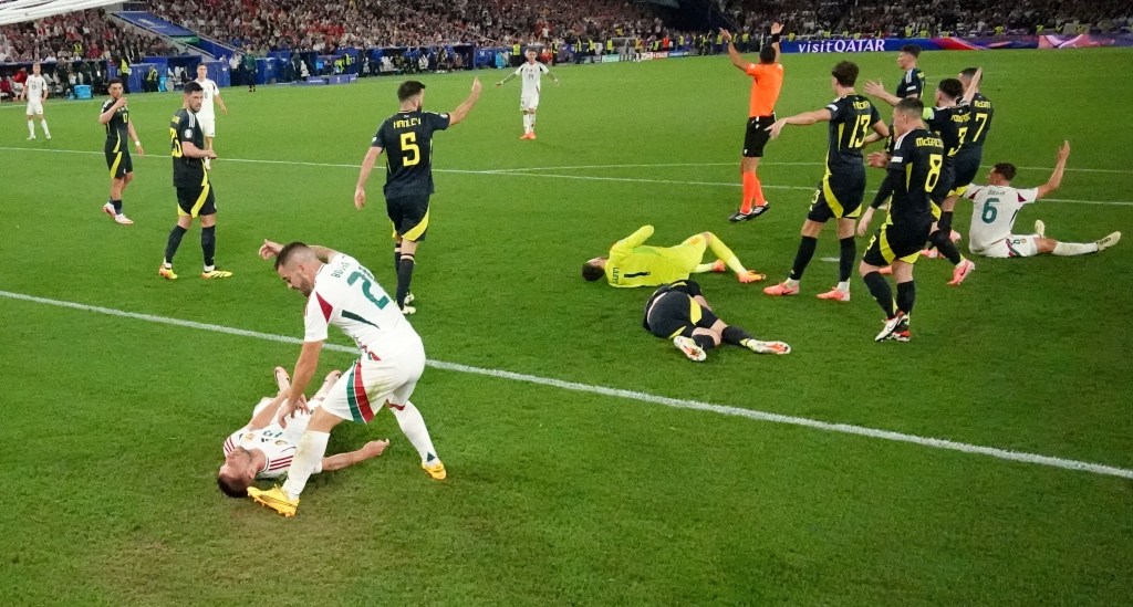 Football players Angus Gunn, Anthony Ralston, and Barnabas Varga reacting after a collision during the Euro 2024 Scotland vs Hungary match at Stuttgart Arena.