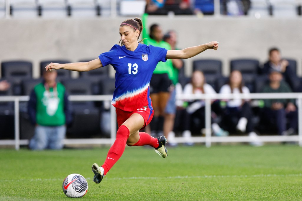 Alex Morgan, wearing a football uniform, shooting a ball across the goal during the SheBelieves Cup final match