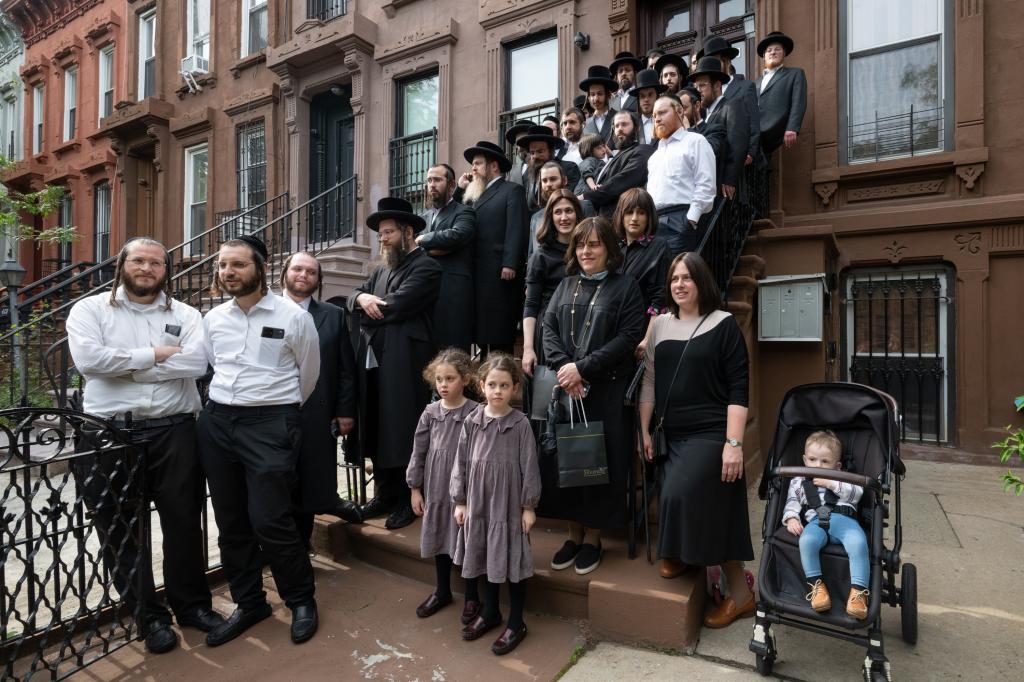 Many Orthodox adults stand on the steps of a brownstone -- the men in top hats and curly sidelocks, the women modestly dressed and three kids in the front.