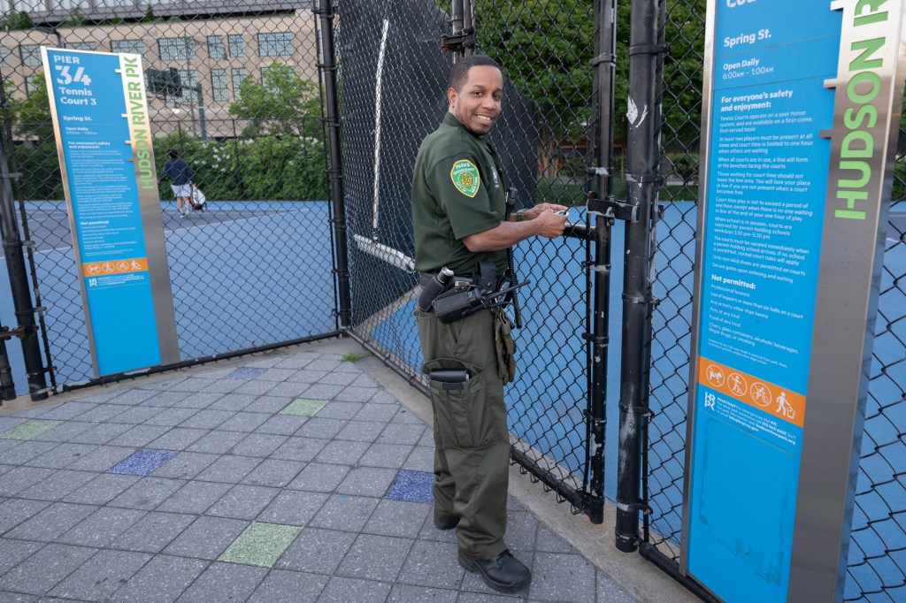 A park official in uniform at Hudson River Park tennis courts, unlocking the gates to the court early in the morning