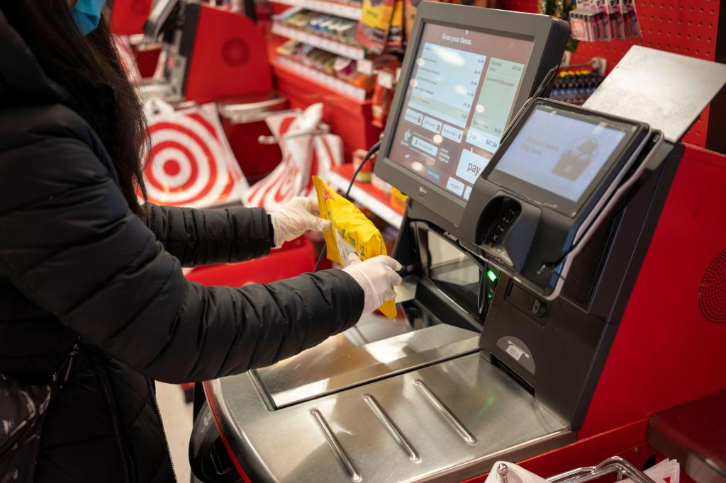Masked shopper in nitrile gloves scanning a bag of Ricola cough drops at a self-checkout in a Target store