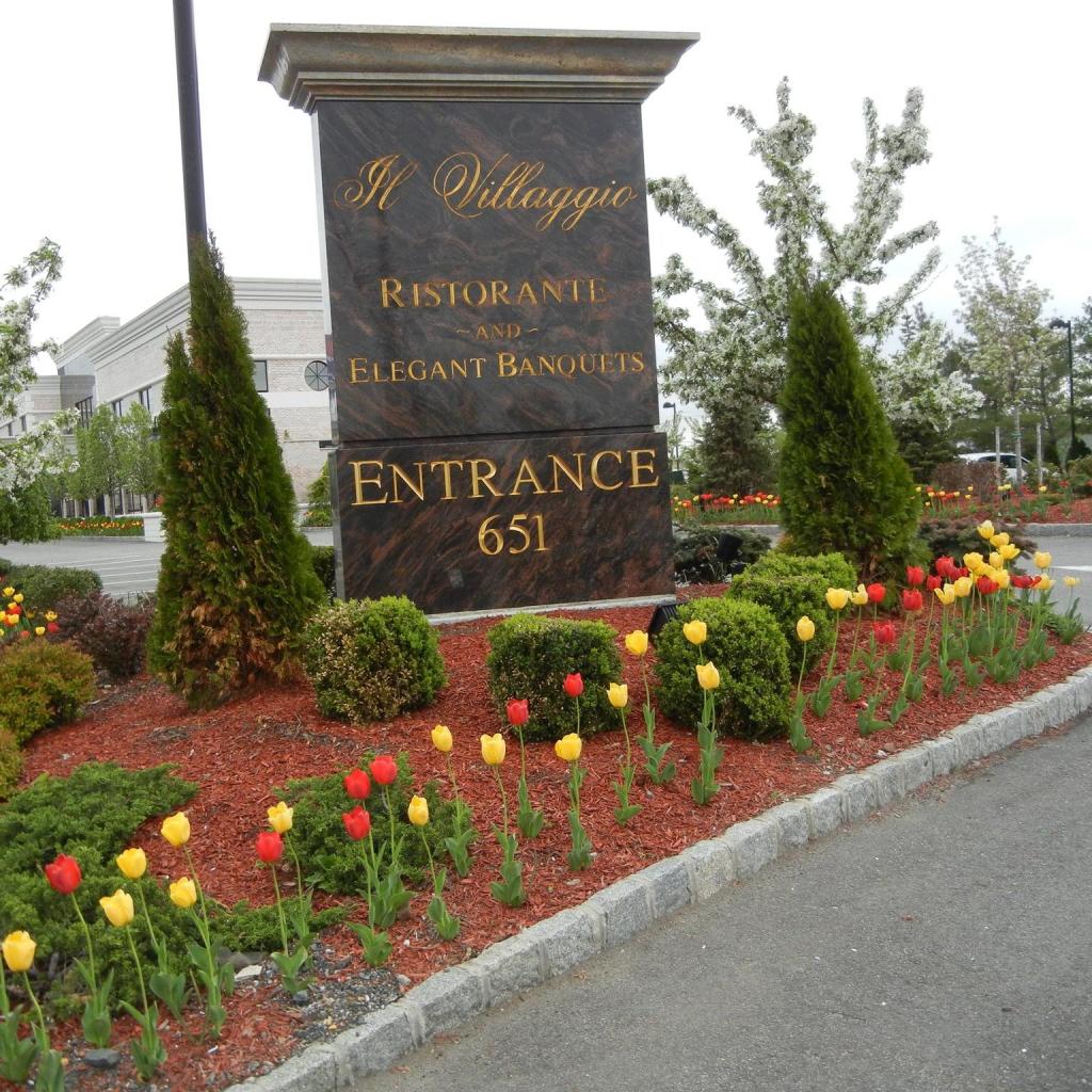 Exterior sign for Il Villaggio Ristorant and Elegant Banquets, sitting on a median landscaped with tulips and bushes