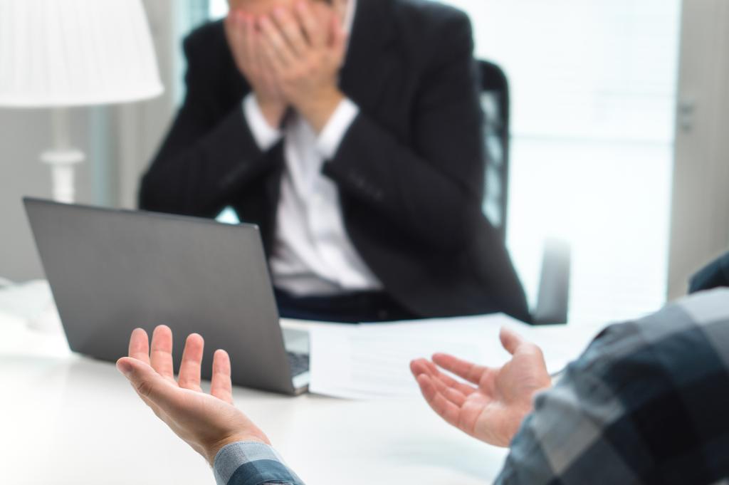 A distressed businessman in a suit covering his face with his hands in an office setting