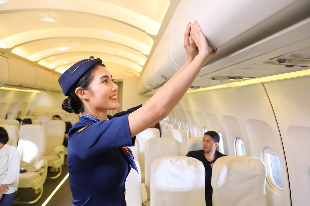 Female flight attendant in blue uniform closing the overhead luggage compartment on an airplane