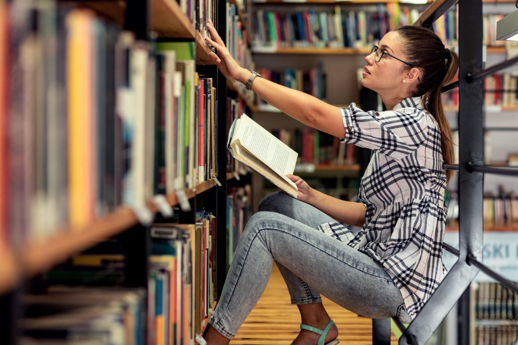 Young female student study in the library reading book while sitting near bookshelf.