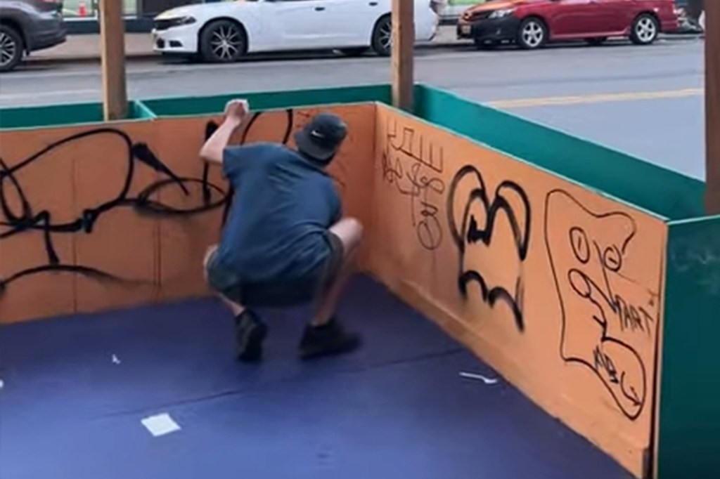 A man crouching inside a dining shed, doing graffiti tagging.