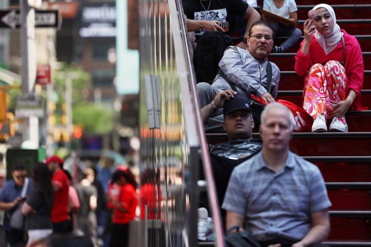 A woman cools herself off with a fan while sitting down in the Time Square area of New York City, U.S., June 18, 2024.