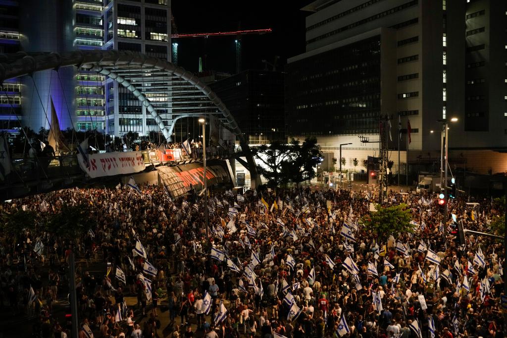 A large crowd of people in Tel Aviv, Israel, holding flags and signs to protest against Israeli Prime Minister Benjamin Netanyahu's government and demand the release of hostages in the Gaza Strip.